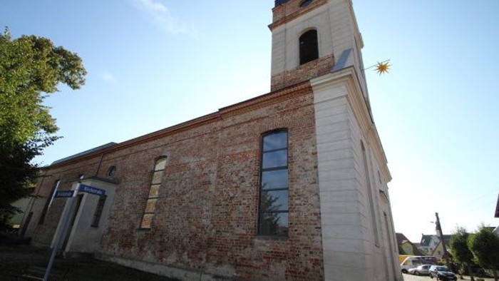 Eine Backsteinkirche mit einem hohen Glockenturm und einem Sternemblem auf dem Dach, vor einem klaren Himmel.