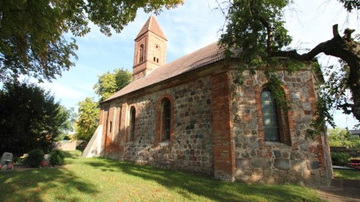 Idyllische Steinkirche, eingebettet in eine ruhige, grasbewachsene Umgebung mit hohem Glockenturm und efeubewachsenen Mauern.