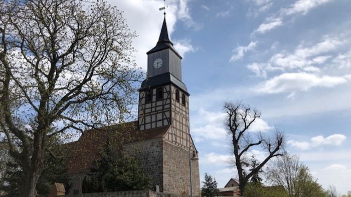 Historische Steinkirche mit hohem Uhrturm und traditionellem Fachwerk-Obergeschoss.