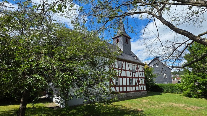 Fachwerkkirche im Hintergrund. Bäume im Vordergrund. Grüne Wiese