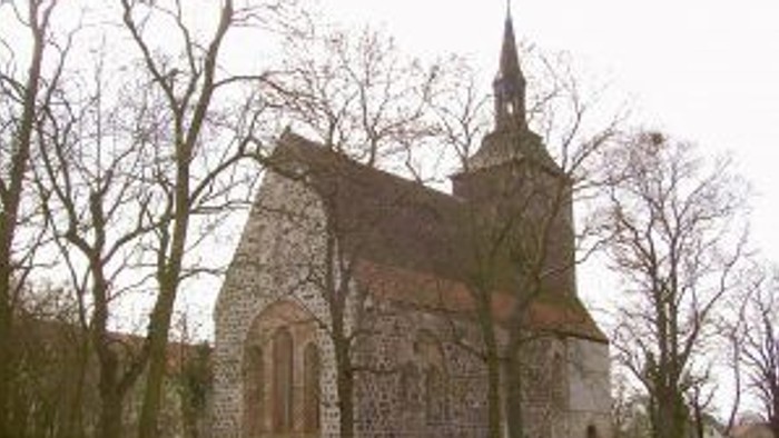 Historische Steinkirche mit hohem Turm, eingebettet zwischen kahlen Winterbäumen und einer Steinmauer.