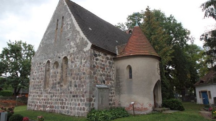 Historische Steinkapelle mit einem kleinen runden Turm und üppiger grüner Friedhofsumgebung.