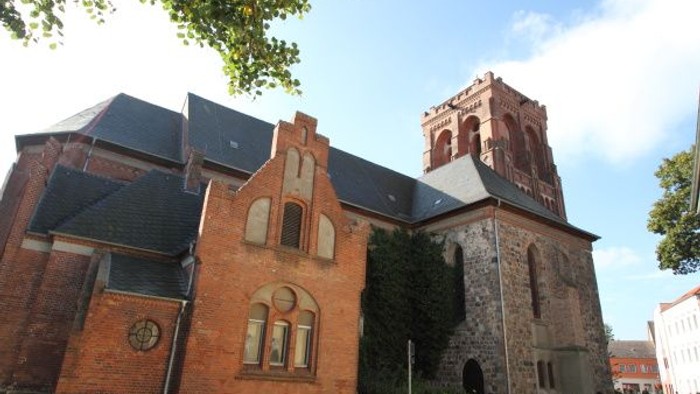 Historische Kirche mit Backstein- und Steinarchitektur, markantem Turm und Bogenfenstern.