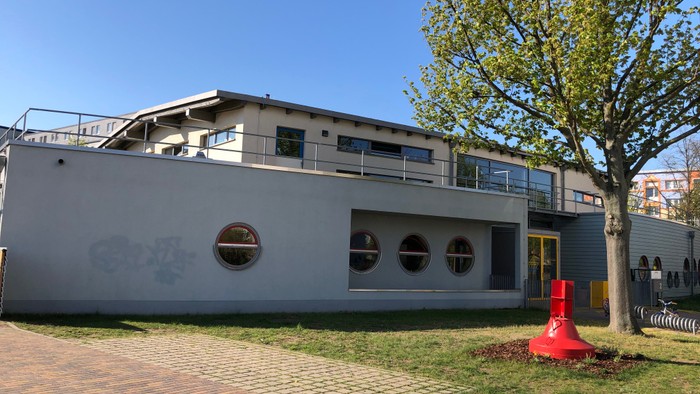 Modernes Gebäude mit runden Fenstern, umgeben von einem angelegten Garten und roten Pflanzkübeln.