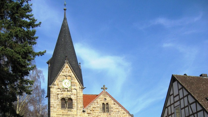 Historische Steinkirche mit hohem Kirchturm und angrenzendem traditionellem Fachwerkhaus.