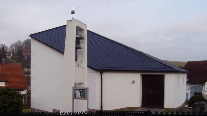 Außenansicht der evangelischen Kirche in Knickhagen. Weiß verputztes Gebäude mit schrägem Dach und freistehendem Glockenturm.