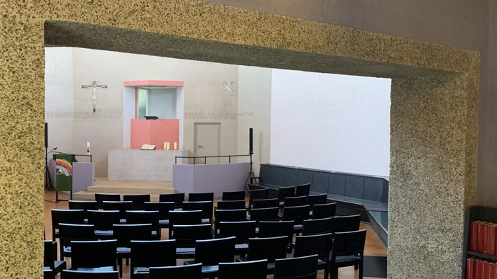 Ein geräumiger Raum mit gestuften schwarzen Stühlen, die als Sitzgelegenheiten angeordnet sind, mit einer strukturierten Wand und einer Bühnenaufstellung.