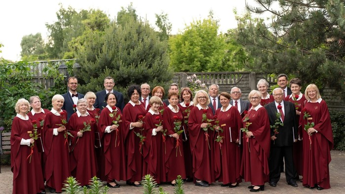 Gruppe in passenden roten Roben mit Blumen, die sich im Freien mit Gästen in eleganter Kleidung fotografieren lassen.