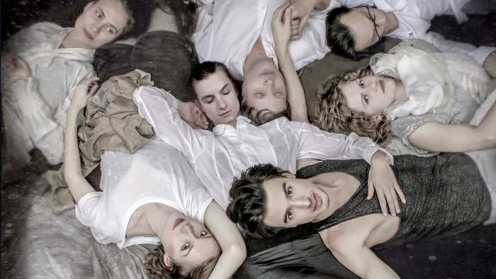 Eine Gruppe von Schauspielern in vintage Kleidung liegt dramatisch auf dem Bühnenboden und wirkt erschöpft oder schlafend.