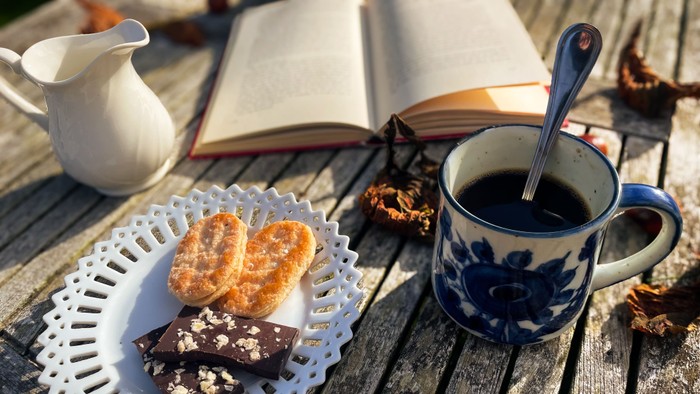 En mugget kaffe og en kage på en træbord med en bog og en kaffepibe