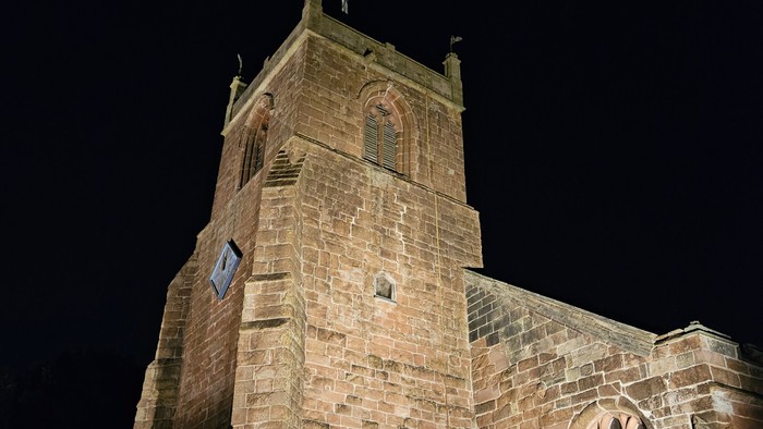 Stone church illuminated at night with a bench in front