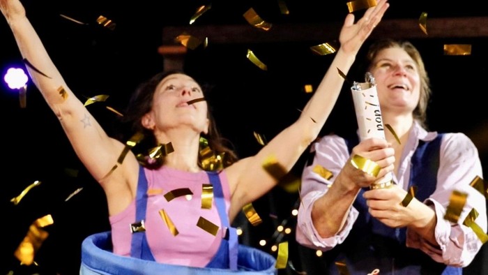 Festlicher Moment mit Konfetti-Regen, während zwei Personen jubeln und Trophäen halten.