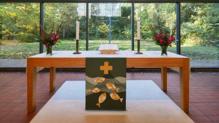 Moderner Kapellenaltar mit großen Fenstern, die die Natur zeigen, geschmückt mit Kerzen und Blumenarrangements.