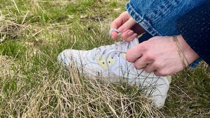 Person binder en hvid sneaker med et farverigt design på en græsklædt udendørs bane.