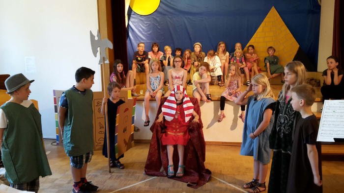 Kinder führen ein Theaterstück mit Kostümen und Requisiten in einer Schul- oder Gemeinschaftstheaterumgebung auf.