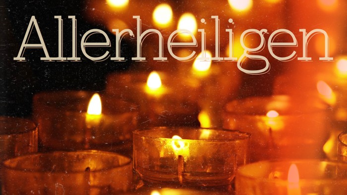 Eine warme Szene mit angezündeten Kerzen und dem Wort „Allerheiligen“, das auf die Feier des Allerheiligenfestes hinweist.