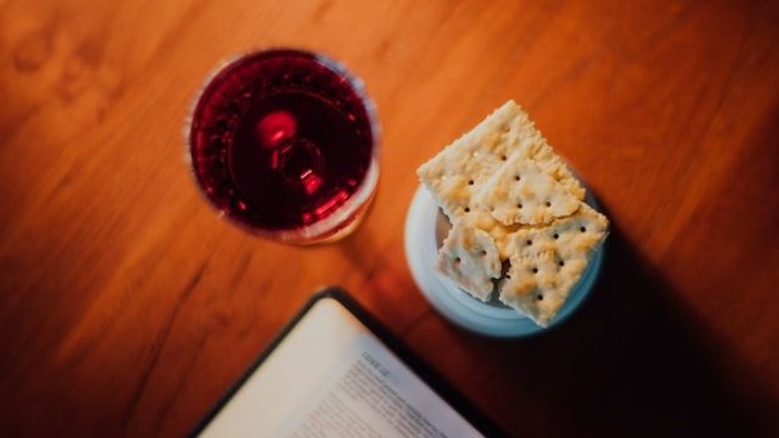 Ein Glas Rotwein und ein Teller mit Crackern auf einem Tisch neben einem aufgeschlagenen Buch