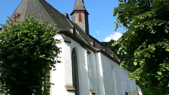 Weiße Kirche mit hohem Turm und spitzen Dach zwischen Bäumen