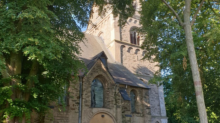 Alte Kirche aus Stein mit hohem Turm und grünem Baum davor