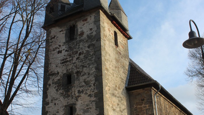 Außenansicht der evangelischen Kirche in Altenhasungen. Hoher Natursteinturm mit mehreren spitzen Schieferhauben.