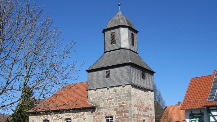 Außenansicht der evangelischen Kirche in Nothfelden. Natursteingebäude mit rotem Ziegeldach und Turm mit schieferverkleideter Haube.