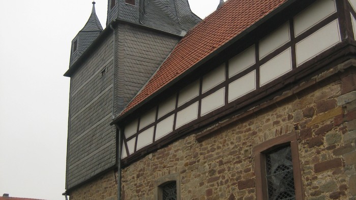 Außenansicht der evangelischen Kirche in Oelshausen. Natursteingebäude mit Fachwerkzone und rotem Ziegeldach.