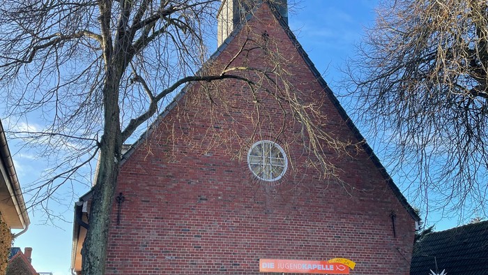 Kleine rote Backsteinkirche mit hohem Turm und Uhr.