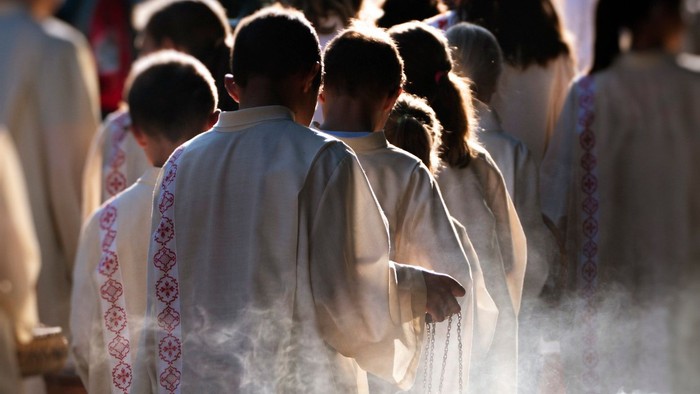 Eine Gruppe von Menschen in weißen Gewändern steht in einer Reihe, einer hält ein Gefäß mit Rauch.