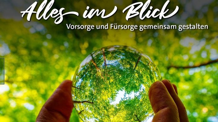 Eine Hand hält eine Kristallkugel, die üppiges Grün reflektiert, mit einem Text, der gemeinsame Weitsicht und Fürsorge fördert.