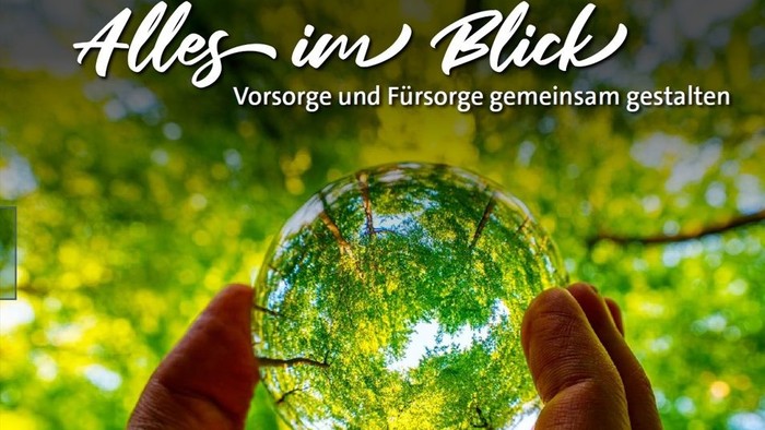 Eine Hand hält eine Kristallkugel, die üppiges Grün reflektiert, mit einem Text, der gemeinsame Weitsicht und Fürsorge fördert.