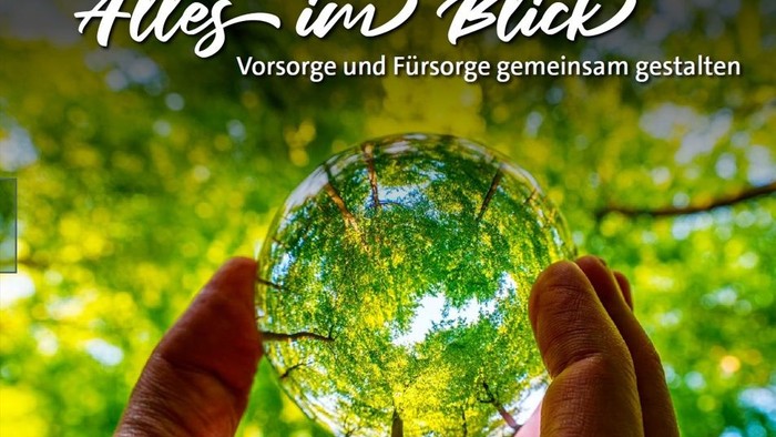 Eine Hand hält eine Kristallkugel, die üppiges Grün reflektiert, mit einem Text, der gemeinsame Weitsicht und Fürsorge fördert.