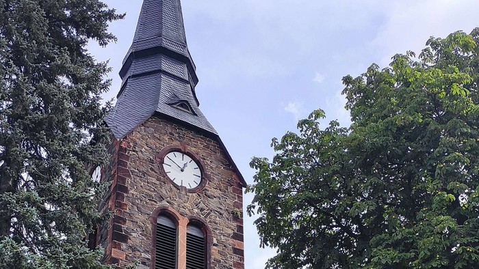 Alte Kirche mit hohem Turm und Uhr, umgeben von Bäumen