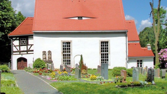 Kleine weiße Kirche mit rotem Dach und schwarzem Turm.