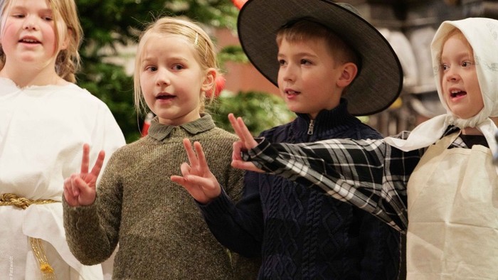 Kinder in historischen Kostümen treten auf der Bühne auf, machen ausdrucksvolle Gesten und singen.