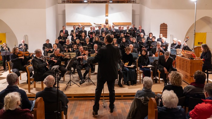 Sinfonieorchester und Chor, die gemeinsam in einer prächtigen Kirche vor aufmerksamem Publikum auftreten.