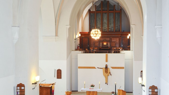 Ein ruhiger Kircheninnenraum mit hölzernen Kirchenbänken, einer erhöhten Orgel und einem Kruzifix über dem Altar.