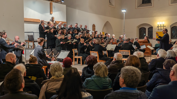 Ein großer Chor und ein Orchester treten gemeinsam in einem geräumigen Innenraum vor aufmerksamen Zuhörern auf.