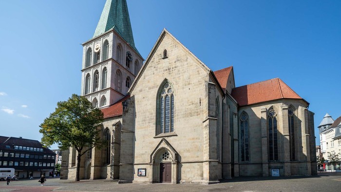 Historische Kirche mit hohem Turm und gotischen Architekturelementen vor einem klaren blauen Himmel.