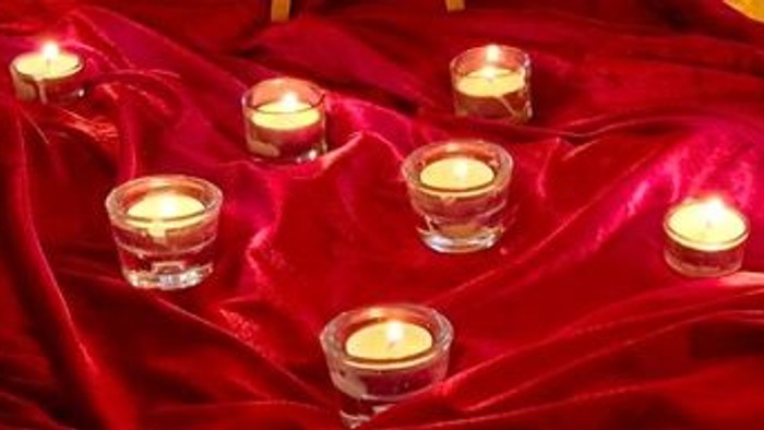 Leuchtende Wachslichter auf rot-glänzendem Tuch.
