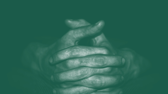 Hænder, der er slørede, foldet sammen i en bønlignende stilling mod en mørkegrøn baggrund.