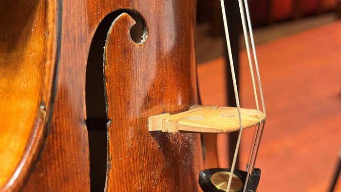 Nærbillede af en poleret cello med synlig stol og strenge i en koncertsal.