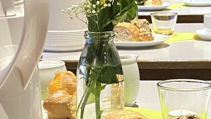 Elegante Buffettafel mit Gebäck, Blumen und verschiedenen Gerichten auf weißen Tellern mit grünen Tischläufern.