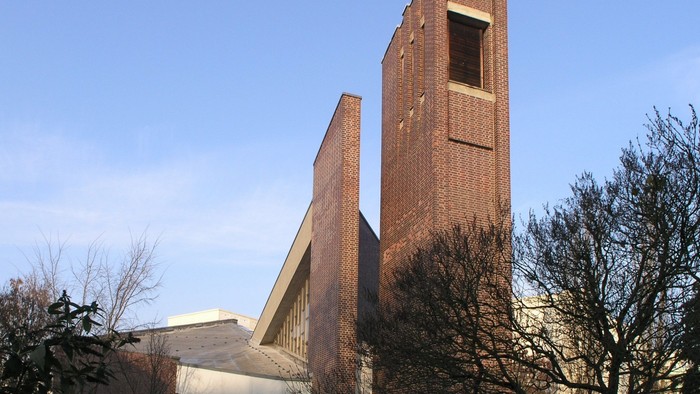 Kirchengebäude mit hohem Turm und Kreuz unter blauem Himmel