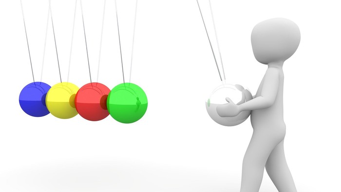 Eine graue Figur hält eine weiße Kugel und schaut vier bunte Kugeln, die an Fäden hängen