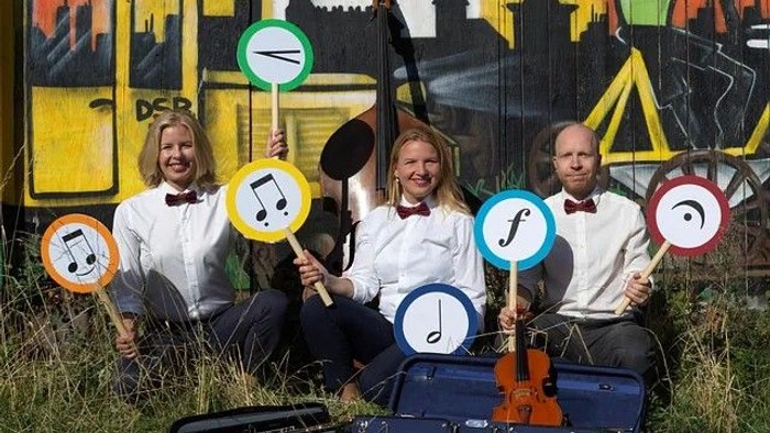 Et musikalsk kvartet poser udendørs med skilte, der viser noder og musikalske symboler, siddende på græsset.