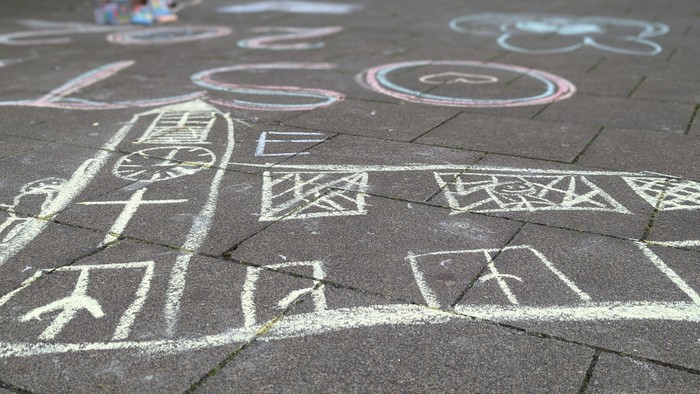 Kreidezeichnungen auf dem Bürgersteig zeigen eine Stadtstraße mit Gebäuden, Autos und Verkehrsschildern.