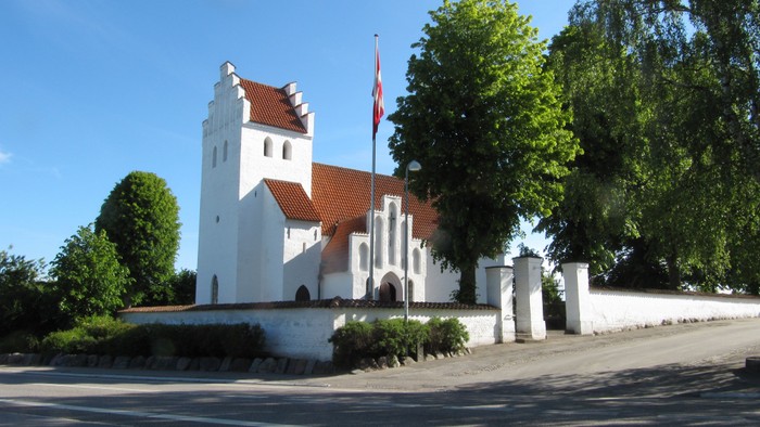 Et hvidt og rødt kirkebygningskompleks med en flaggstang foran