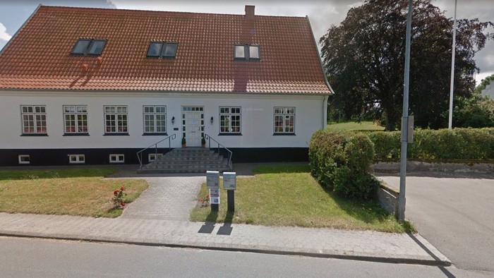 En hvid og sort toetages hus med rødt tag og en trappe op til indgangen.