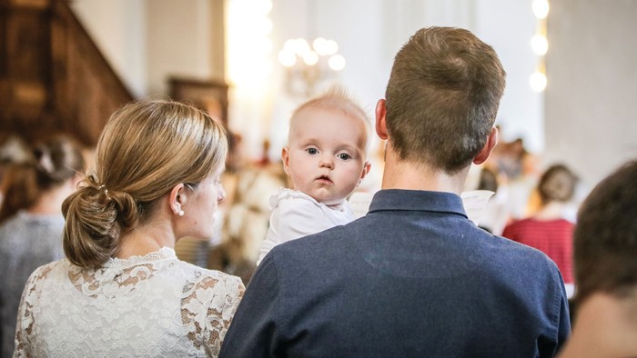 En familie i kirke, mor og far holder deres barn oppe.