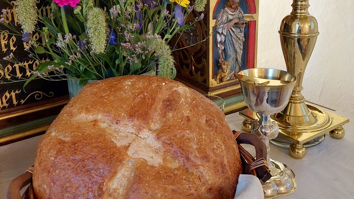Helligt brød i en kurv med blomster, religiøse ikoner og ceremonielt guldsmykke på et bord.